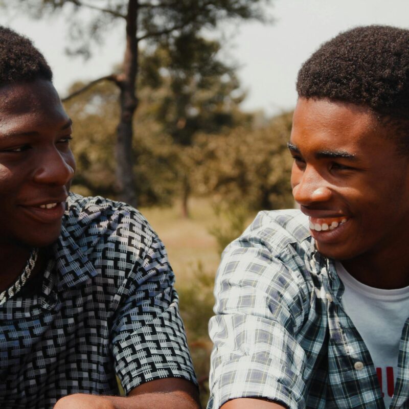 Two young men smiling and enjoying a sunny day outdoors, engaging in friendly conversation