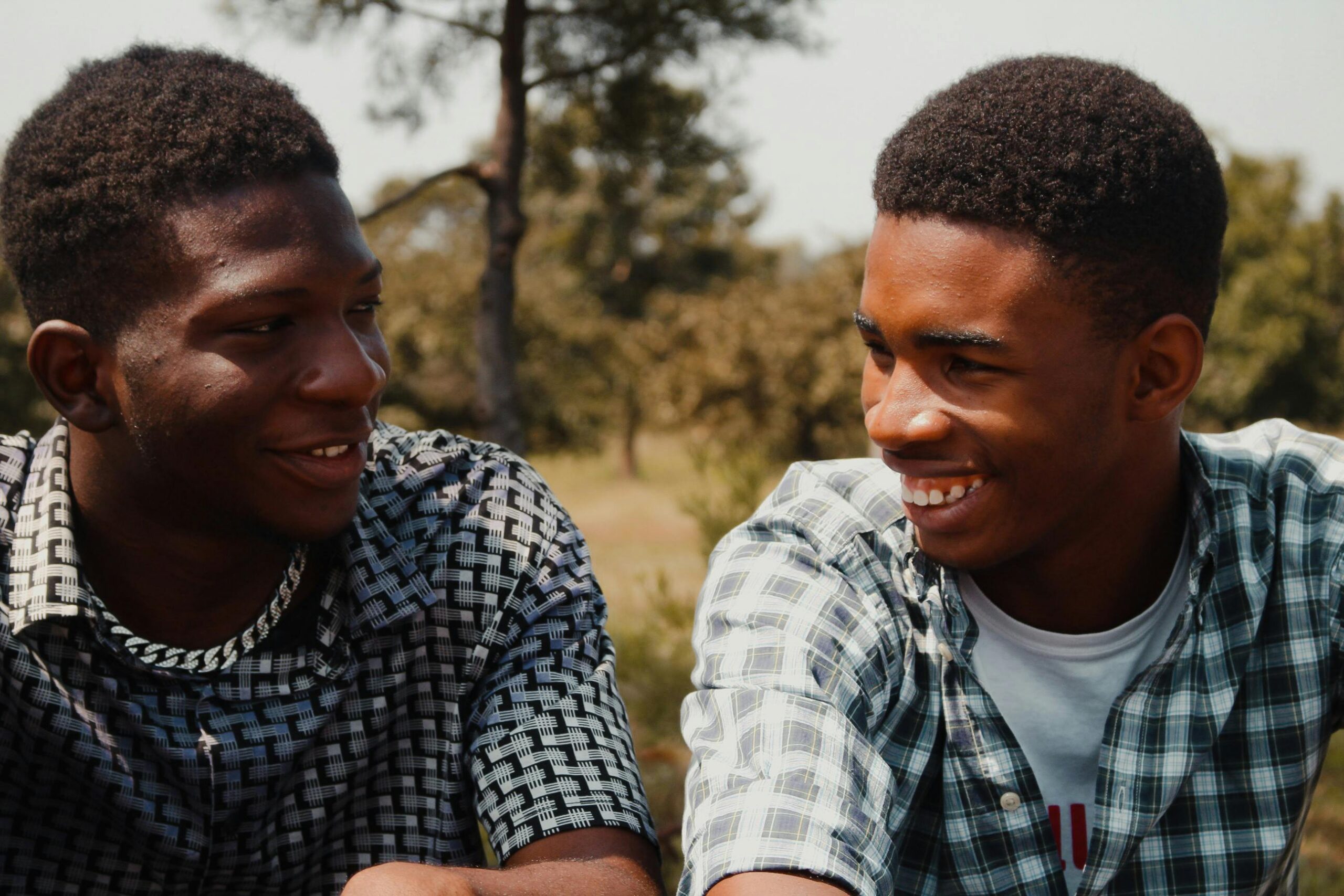 Two young men smiling and enjoying a sunny day outdoors, engaging in friendly conversation